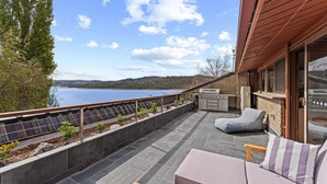Un patio con vista a un lago, una parrilla y una zona de estar con cojines.