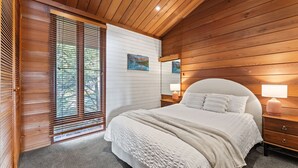 Un dormitorio con una cama grande, paredes de madera, una ventana con persianas y una mesita de noche con lámpara.