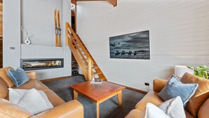 Una sala de estar moderna con sofás de cuero, una mesa de centro de madera, chimenea, escalera y un cuadro en la pared.