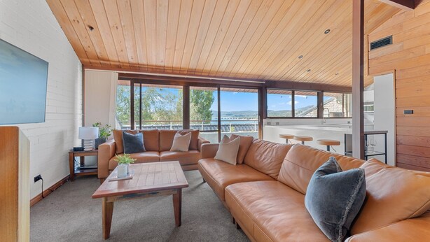 Una sala de estar moderna con techo de madera, ventanas amplias, un sofá de cuero, una mesa de centro y vistas al exterior.