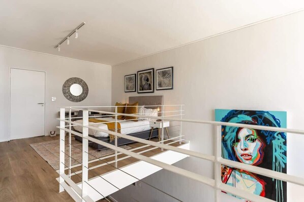 Une chambre avec un lit superposé, un miroir rond et trois œuvres d’art encadrées accrochées au mur.