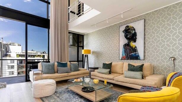 A modern living room with a glass coffee table, beige sofas, and a yellow armchair.