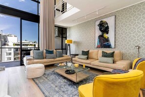 Un salon moderne avec une table basse en verre, des canapés beiges et un fauteuil jaune.