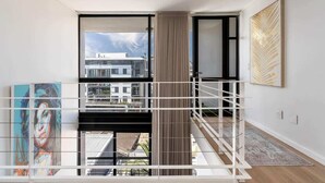 A modern interior with a balcony, large windows, and a view of buildings.