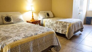 Two beds with patterned bedspreads, a bedside table with a lamp, and a window with a view of the outside. - The Hamlet Suites - Bright and spacious Studio Apartment 1 (Gros Islet)