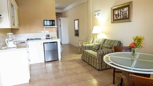 A compact living space with a kitchenette, a dining area with a glass table, and a seating area with a couch. - The Hamlet Suites - Bright and spacious Studio Apartment 1 (Gros Islet)