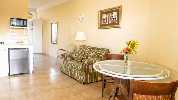 A compact living space with a kitchenette, a sofa, a dining table, and a lamp. - The Hamlet Suites - Bright and spacious Studio Apartment 1 (Gros Islet)