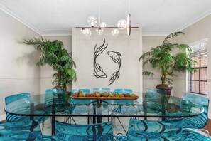 A round glass table with blue chairs, a wooden tray with food, and a wall art piece. - Huge 8BR w/HTD Pool, Ensuites, Games, Near Beach (Palm Harbor)