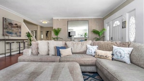 A living room with a sectional sofa, a coffee table, and a TV. There are potted plants and a painting on the wall. - Huge 8BR w/HTD Pool, Ensuites, Games, Near Beach (Palm Harbor)
