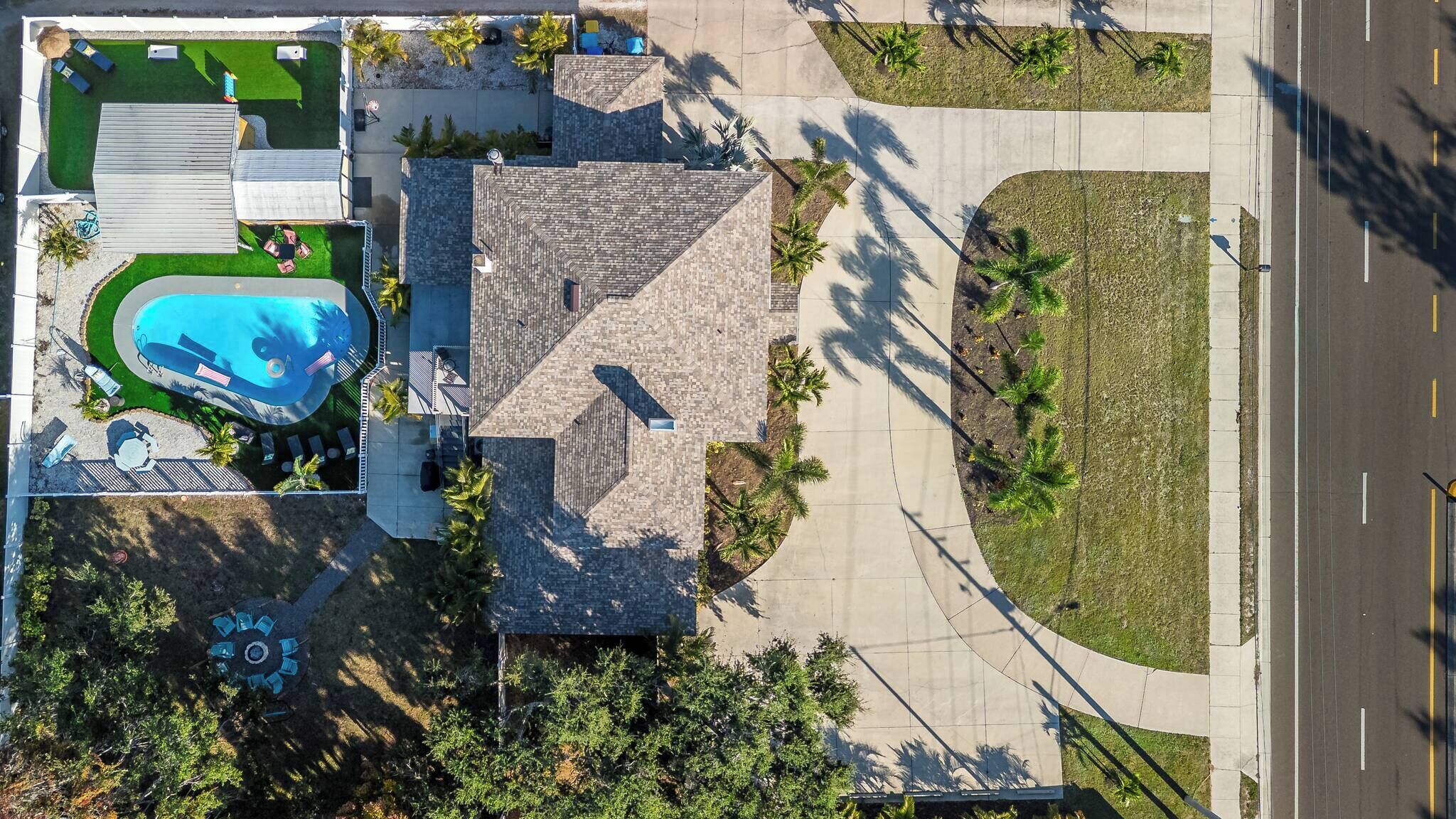 An aerial view of a property with a swimming pool, a patio area, and a road adjacent to the property.