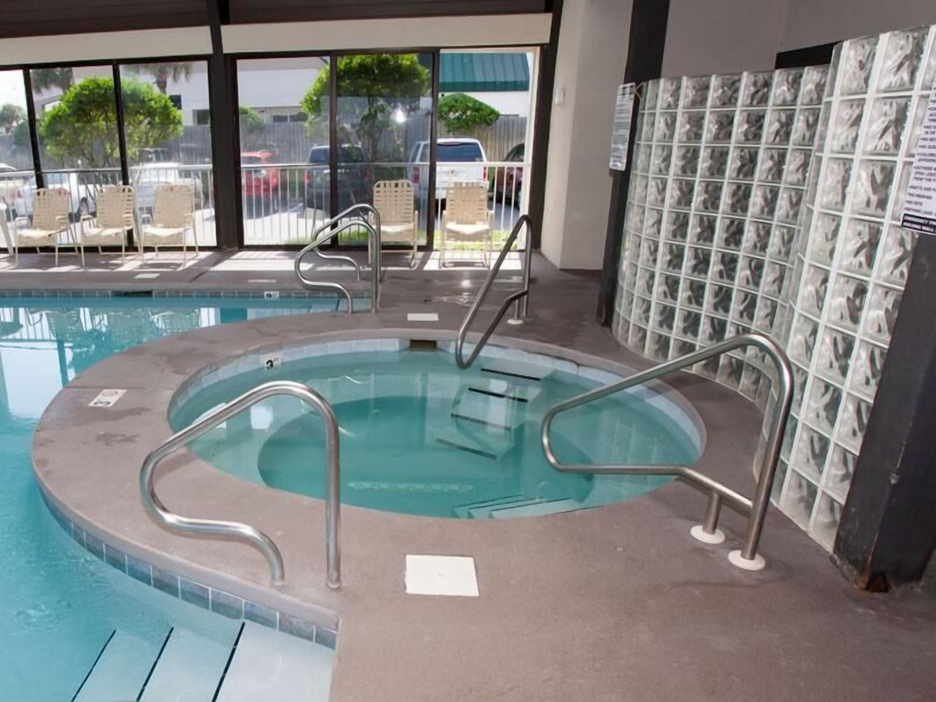 An indoor swimming pool with a hot tub, lounge chairs, and a tiled wall.