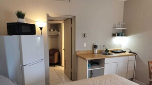 Une chambre d’hôtel de taille réduite, comprenant un lit, une kitchenette, une petite salle de bain et une porte donnant sur un placard.