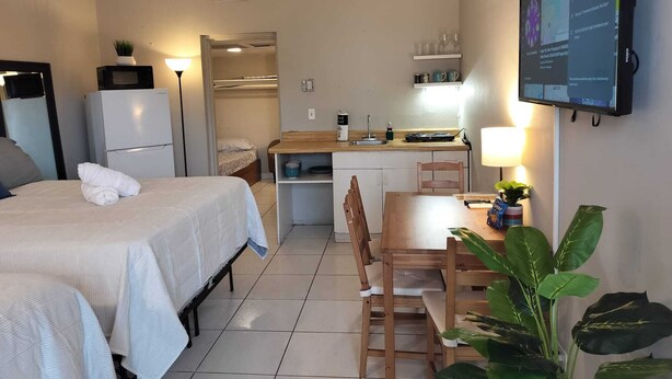 Une chambre d’hôtel compacte comprenant un lit, une table de chevet, une petite kitchenette, un coin repas et un téléviseur fixé au mur.