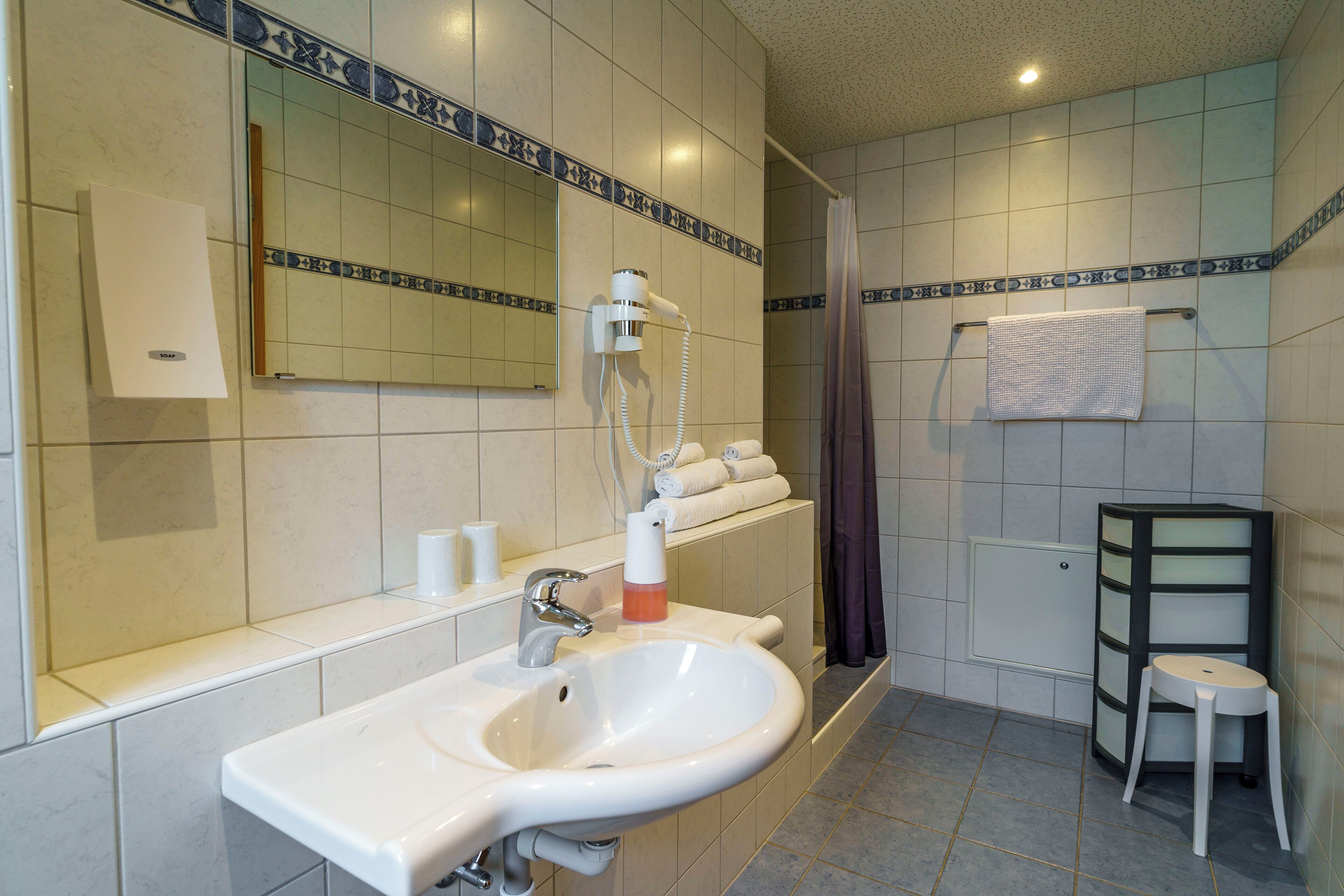 A bathroom with a sink, mirror, towel rack, and shower curtain.