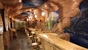 A restaurant with wooden tables and chairs, a mural of a mountainous landscape, and hanging lights. - Seeblick Hotel und Restaurant Rössli (Quarten)