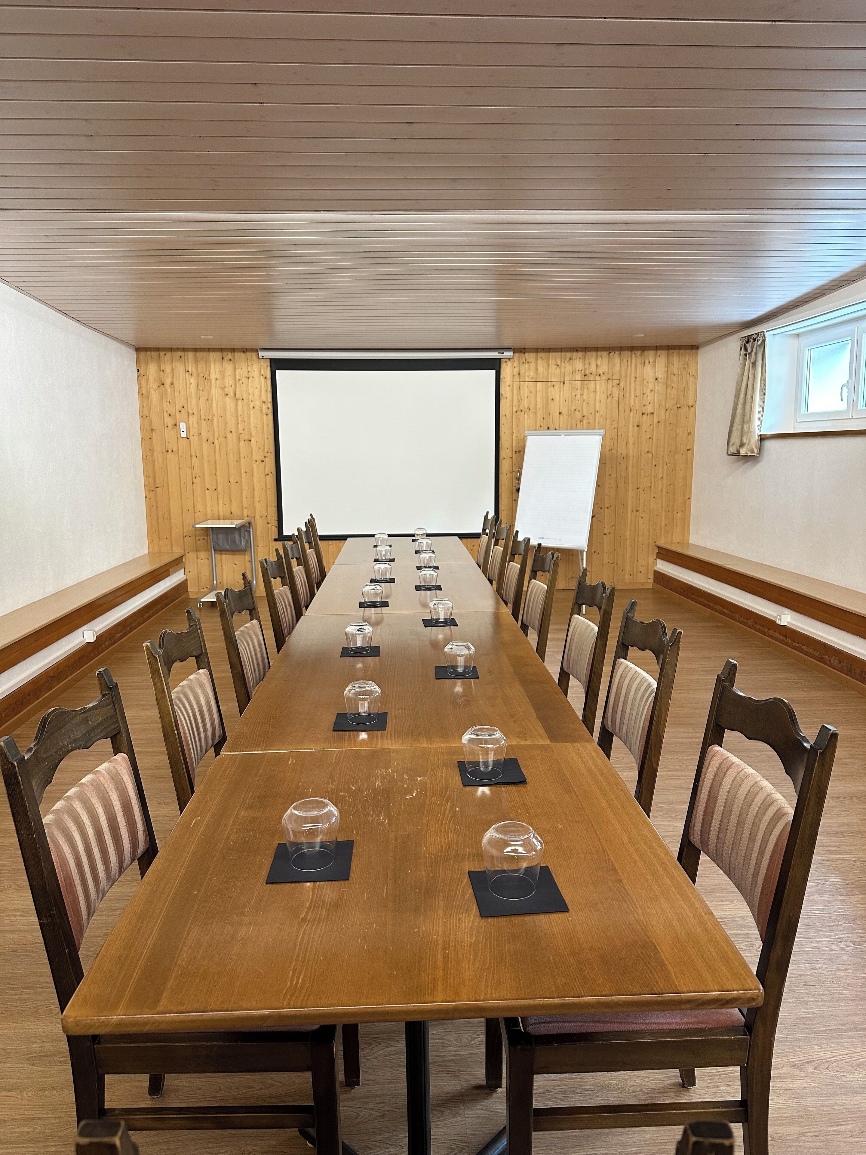 A conference room with a long wooden table, chairs, a projector screen, and a whiteboard.
