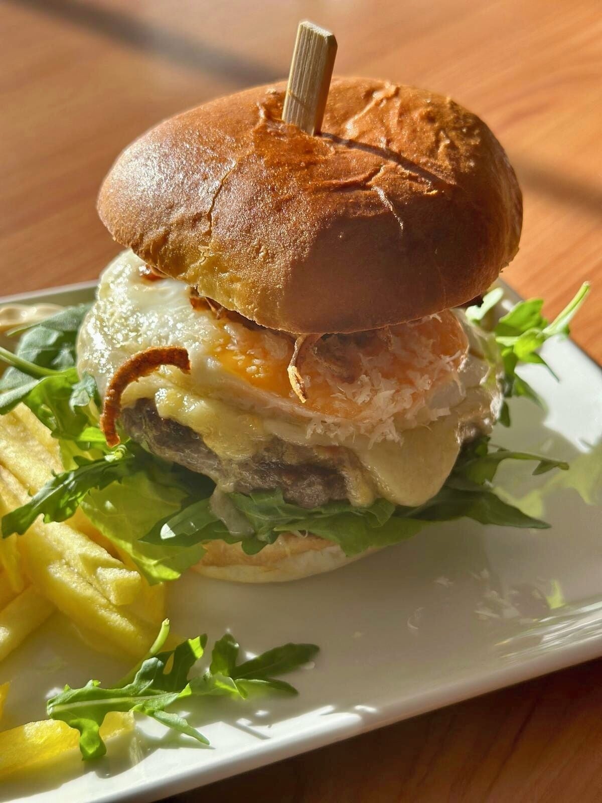 Un sandwich préparé avec un pain grillé, de la laitue, du fromage et un œuf frit, servi avec des frites dans une assiette blanche.