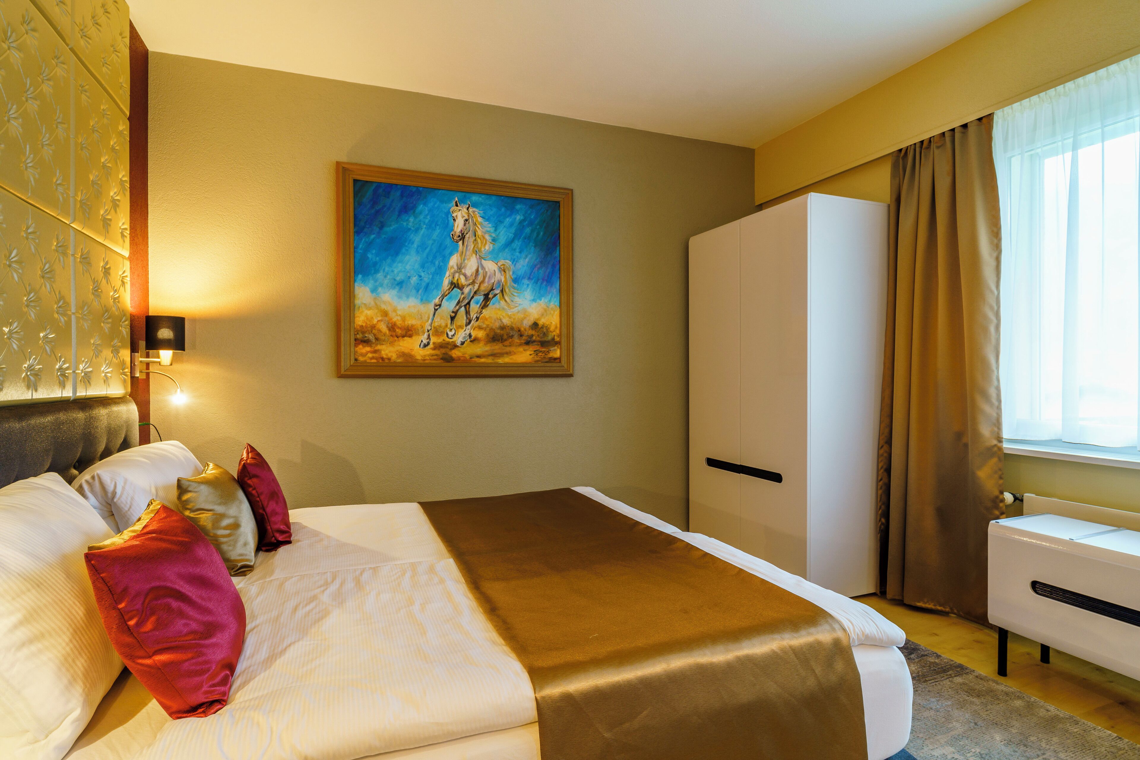 Una habitación de hotel con una cama grande, un cuadro de un caballo, un armario y una ventana con cortinas.