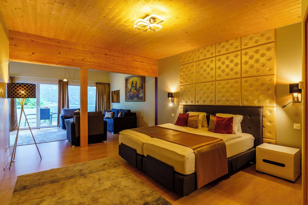 A spacious bedroom with a large bed, a nightstand, and a built-in headboard with a floral pattern.