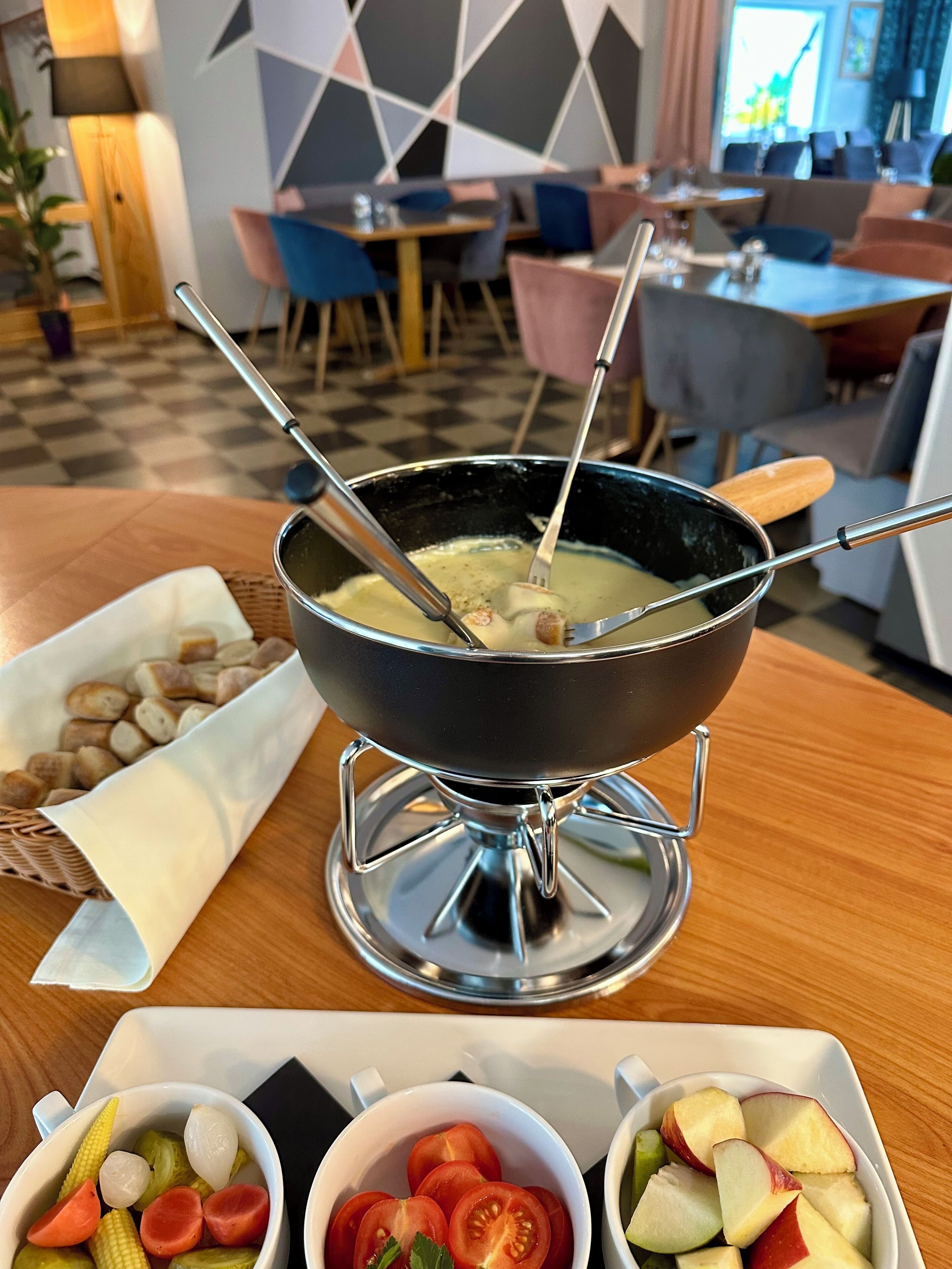 Una mesa de comedor con una olla para fondue, una cesta de pan y tazones de verduras.