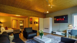 A modern living room with a sofa, armchairs, a coffee table, and a TV displaying 'NETFLIX'. - Seeblick Hotel und Restaurant Rössli (Quarten)