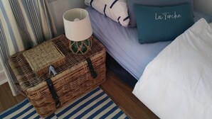 Une chambre à coucher avec un lit, un panier en osier contenant une lampe et un oreiller sur lequel est inscrit le mot « La Torche ».