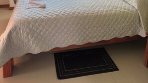 Un lit avec une couette blanche matelassée, des rideaux verts et un paillasson noir.