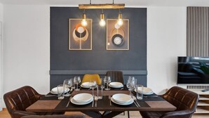 Ein moderner Essbereich mit einer dunklen Wand, zwei gerahmten Kunstwerken und einem Holztisch, gedeckt für sechs Personen.
