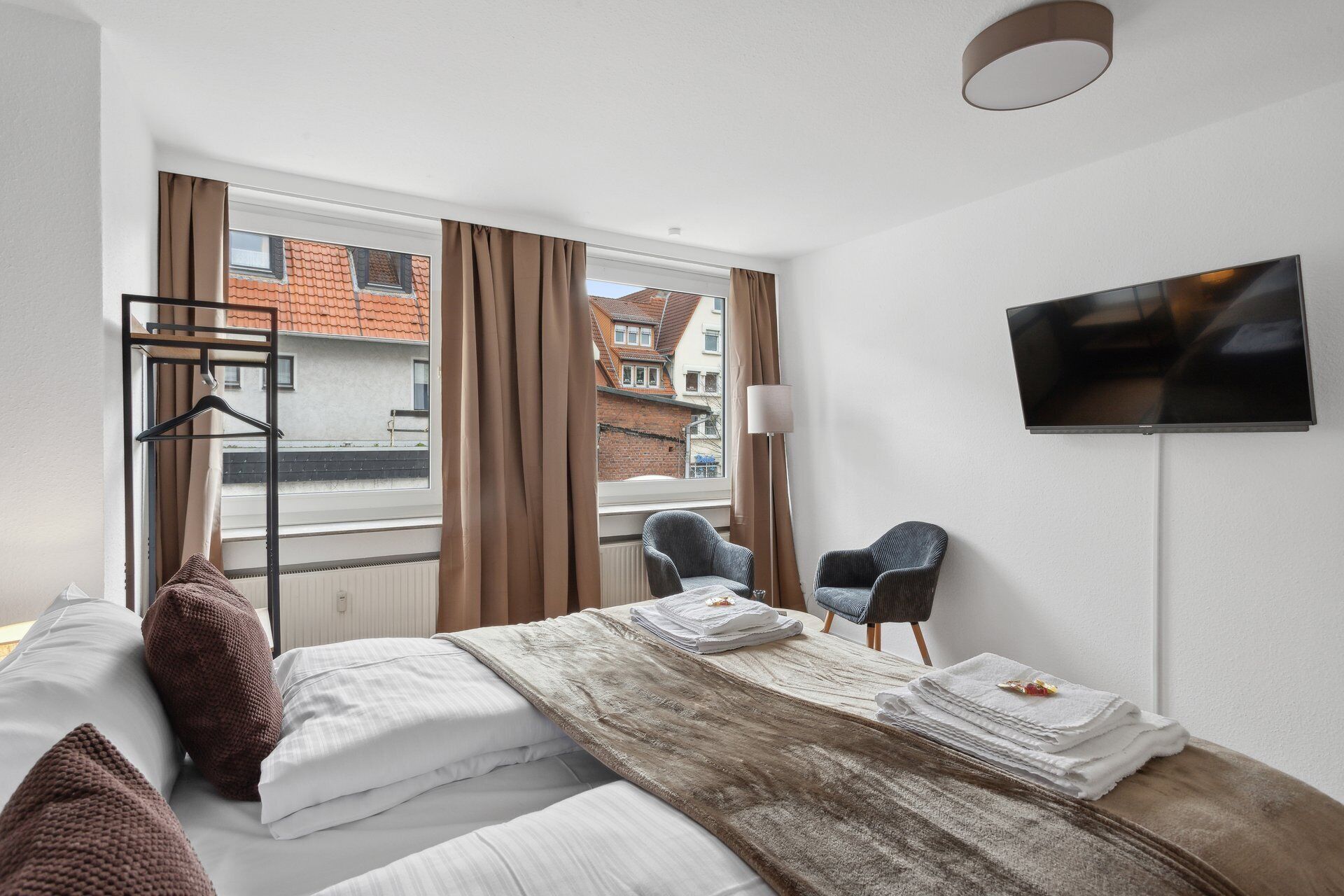Una camera d'albergo con un letto, due poltrone, una televisione e una finestra con tende.