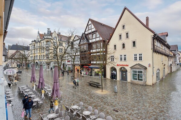 Una plaza adoquinada con arquitectura europea tradicional, mesas al aire libre y diversas tiendas.