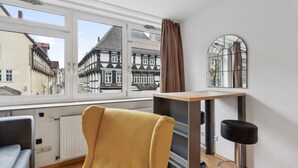 Ein Zimmer mit einem großen Fenster, einem gelben Sessel, einem Holztisch und einem schwarzen Barhocker.