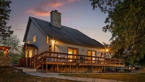 Une maison à deux étages avec une cheminée en pierre, une terrasse en bois et un mur en pierre.