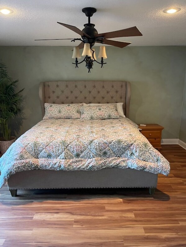 A bedroom with a tufted headboard, a floral-patterned bedspread, a ceiling fan, and a nightstand with a lamp.