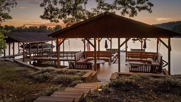 Un belvédère en bois, doté de bancs et de tables, surplombe un plan d’eau et est entouré d’une végétation naturelle.