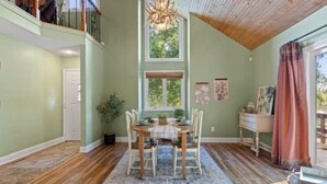 Un espace repas comprenant une table et des chaises en bois, un lustre et une vue sur l’extérieur.