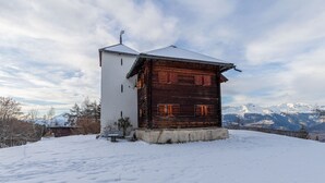 A wooden cabin with a white exterior and a snow-covered roof, surrounded by a snowy landscape and mountains in the background. - Supersaxo QUIET & CHARMING chalet 10 pers (Veysonnaz)