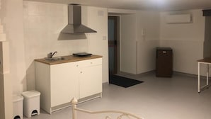 A compact kitchen with white cabinets, a stainless steel sink, and a black range hood. There is a small trash bin and a black mat on the floor. - B&B il girasole (Maddaloni)