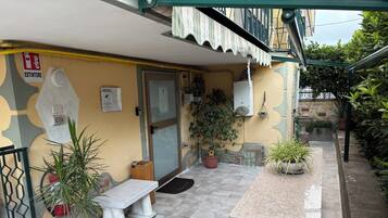 A small outdoor area with a bench, potted plants, a door, and a fire extinguisher sign.