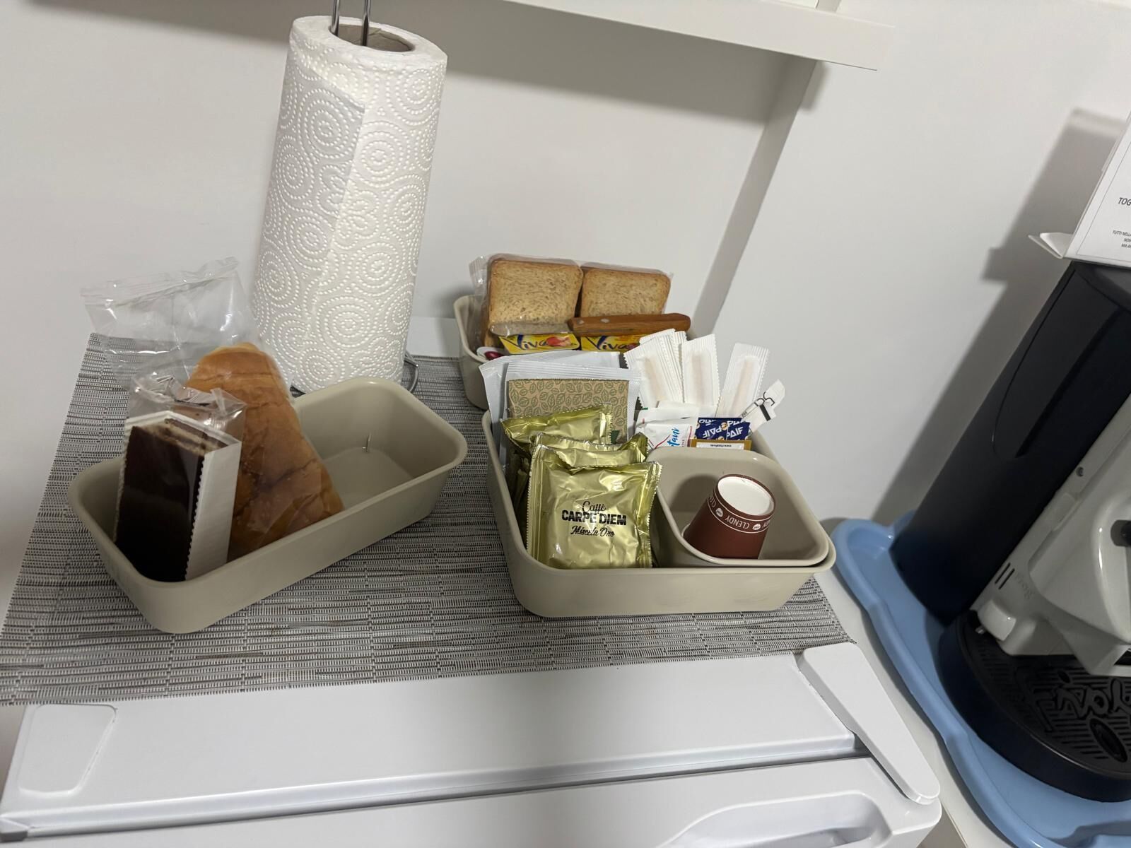 A breakfast tray with bread, a chocolate bar, a bag of chips, a cup of coffee, and a roll of paper towels.