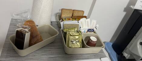 A breakfast tray with bread, a chocolate bar, a bag of chips, a cup of coffee, and a roll of paper towels.