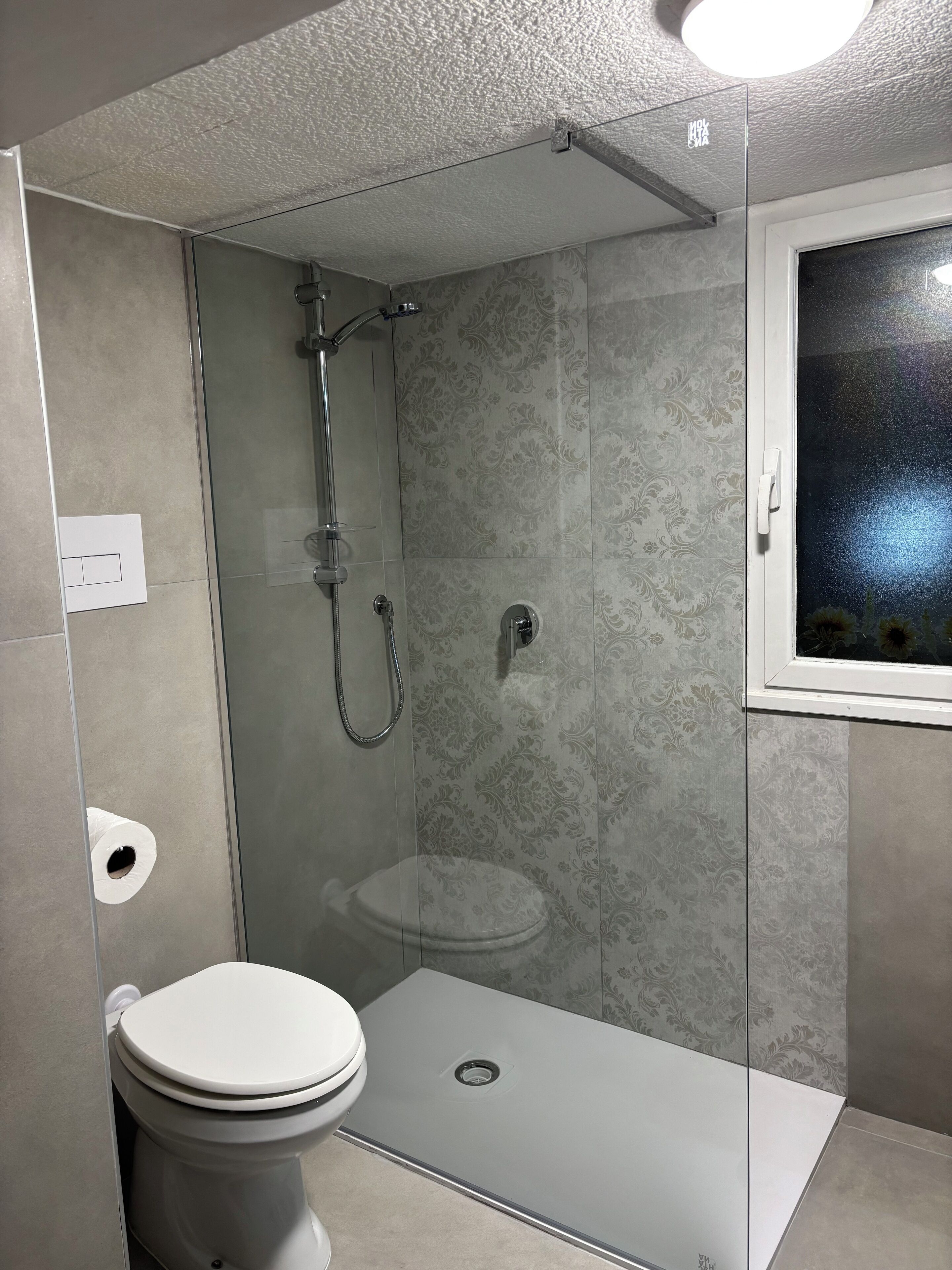 A modern bathroom with a shower enclosure, toilet, and a small window.
