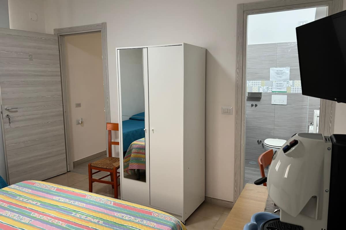 A bedroom with a bed, a wardrobe, a chair, a desk, and a television.