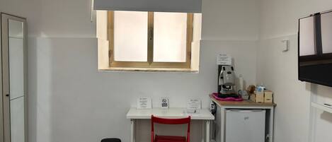Una habitación pequeña y limpia con una cama, un escritorio, una silla, una cafetera y un refrigerador.