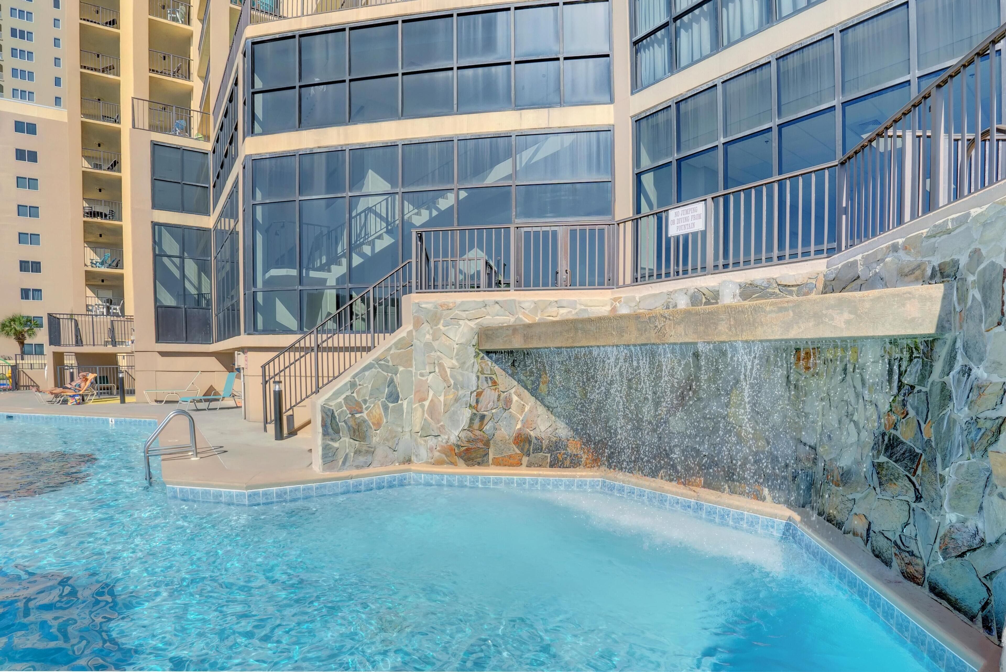 Una piscina amb una paret de pedra i una escala que condueix a un balcó.
