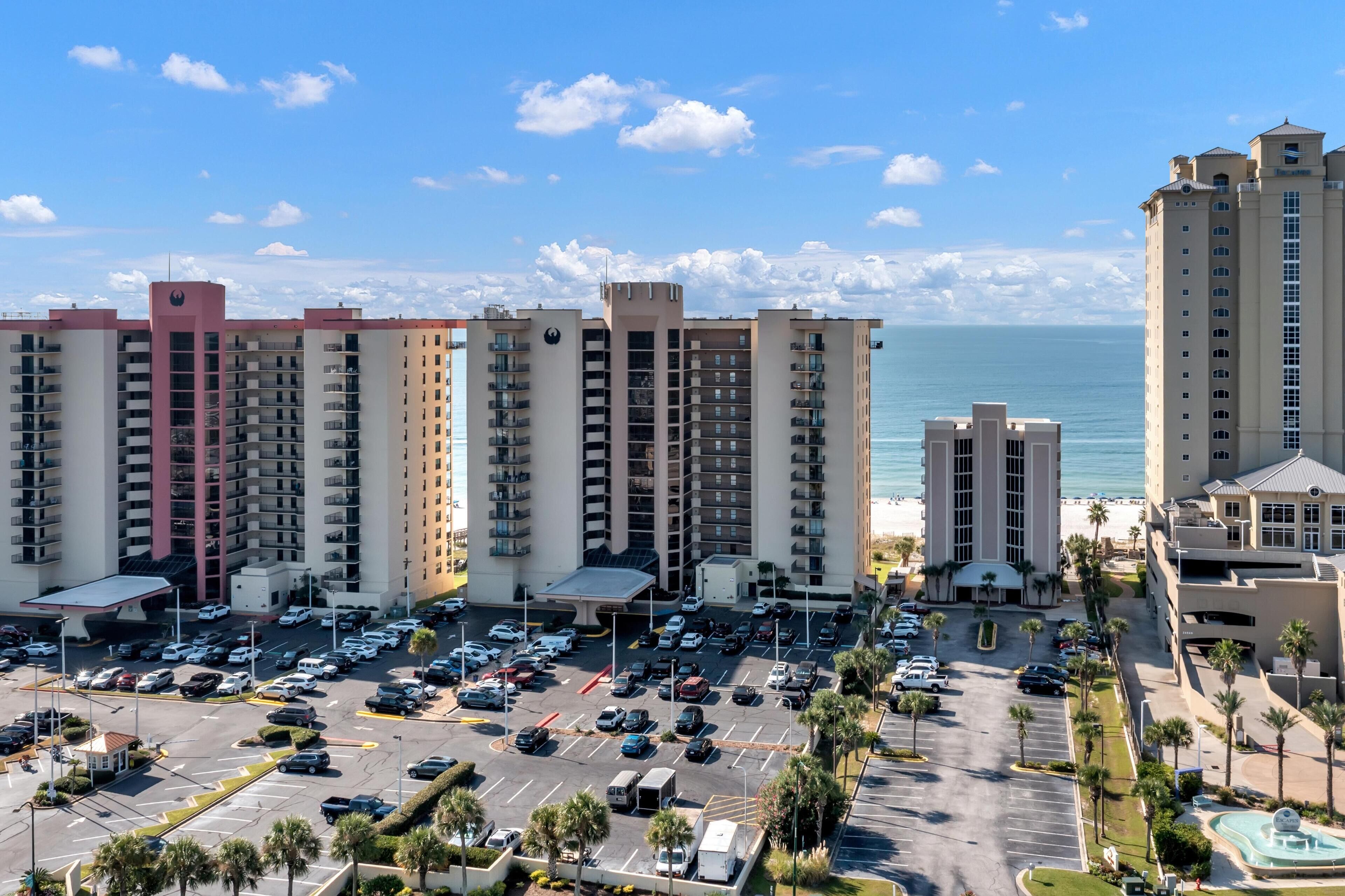 Un hotel moderno con numerosi balconi, un parcheggio e vista sull'oceano.