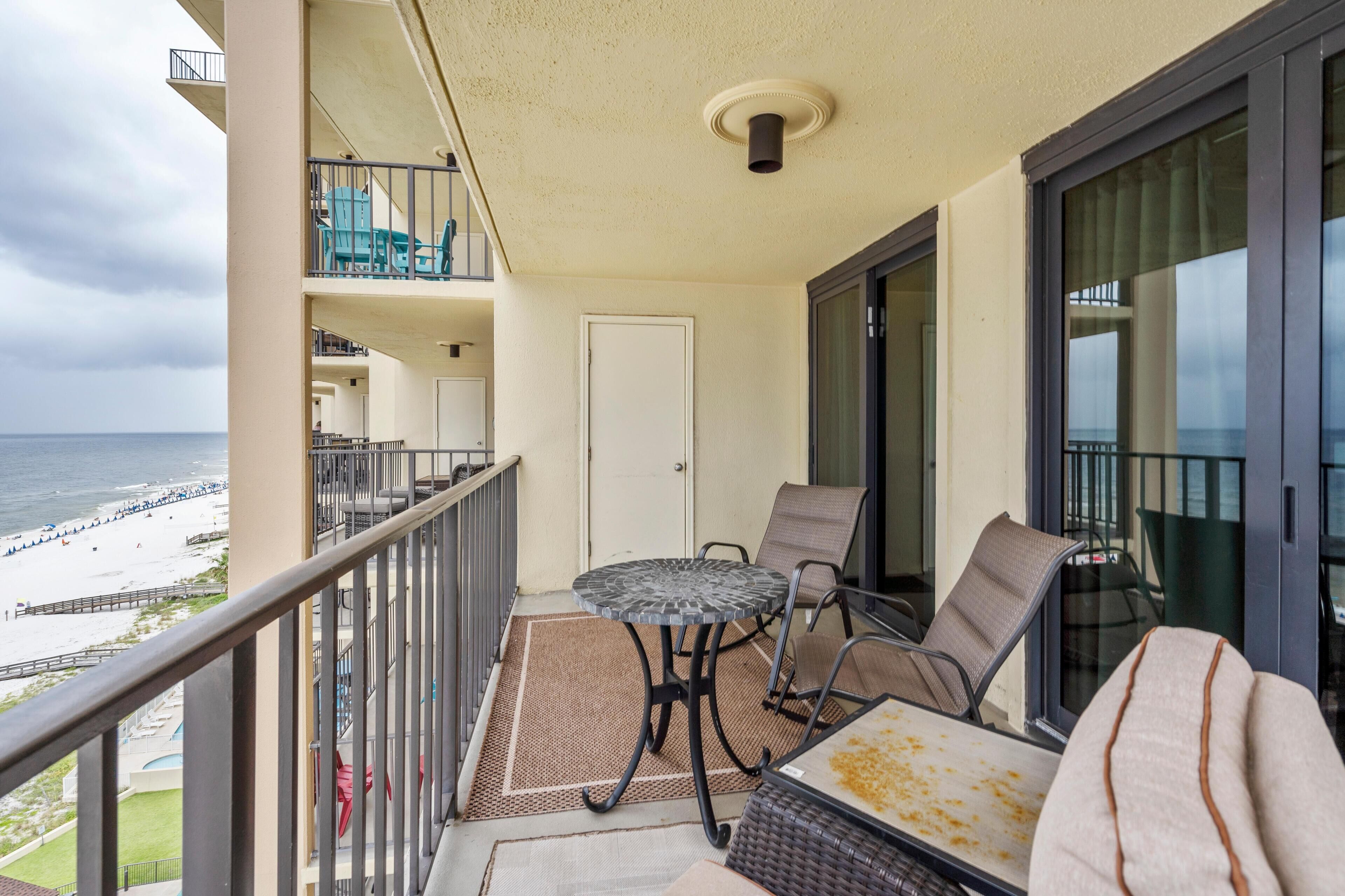 A balcony with a table and chairs, overlooking a beach.