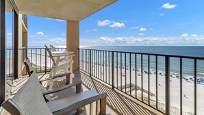 A balcony with a view of a beach, featuring a railing, a table, and chairs. - Phoenix I 1097 (Orange Beach)