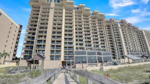 A high-rise residential building with multiple balconies, a covered walkway, and a glass facade. - Phoenix I 1097 (Orange Beach)