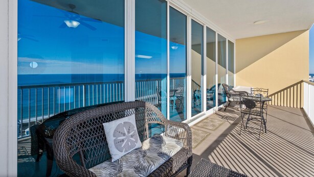 A balcony with a wicker sofa and table, large glass doors, and a view of the ocean.