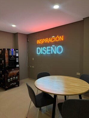Une salle de conférence avec un panneau néon sur lequel on peut lire « INSPIRACIÓN DISEÑO » et un distributeur automatique.